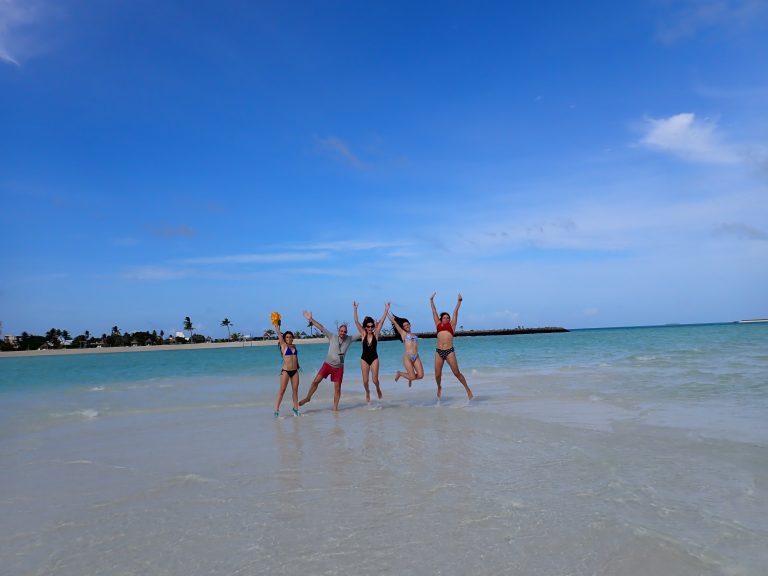 Grupo de viajeros saltando en una playa de Maldivas mientras les fotografían