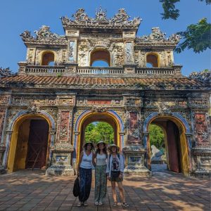 Tres mujeres viajeras que llevan puesto el sombrero típico vietnamita posando delante de la entrada de la Ciudad Imperial de Hue en Vietnam